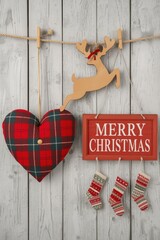 A Christmas holiday arrangement featuring a red plaid heart pillow, a small wooden reindeer cutout, a framed "MERRY CHRISTMAS" sign, and three miniature hanging stockings, all set against a rustic whi
