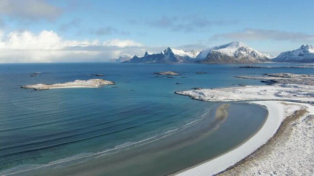 A drone captures the snowy winter beach at Fredvang in the Lofoten Islands, where turquoise waters meet white sand under a deep steel-blue sky - surreal and breathtaking.