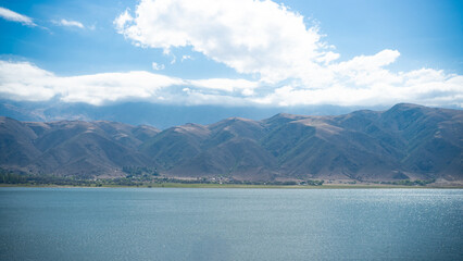 Wooden dock pier extending into calm mountain lake with clear blue sky and scenic alpine mountain range panorama in background under bright sunlight