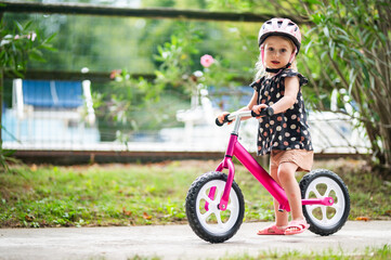 Toddler Girl Wearing a Helmet and Riding a Bright Pink Balance Bike Outdoors