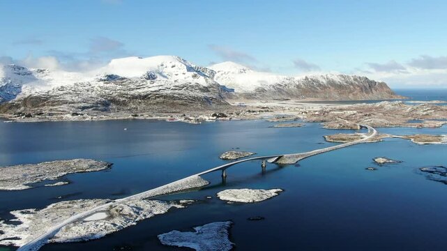 Aerial drone view of the bridges between Ramberg and Fredvang in the Lofoten Islands, crossing steel-blue waters and snowy winter landscapes in a calm, soothing atmosphere.