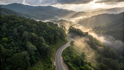 High-altitude cinematic shot of a serpentine mountain road cutting through an emerald tropical rainforest, early morning fog drifting between treetops, dramatic light rays piercing the mist, untouched