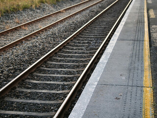 Fototapeta premium The train tracks are empty and the train is not in sight. The tracks are made of metal and are covered in gravel. Platform on the right and dangerous zone marked by yellow line.