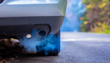 Car Emitting Blue Smoke from Exhaust Pipe on a Wet Roadside, Symbolizing Pollution