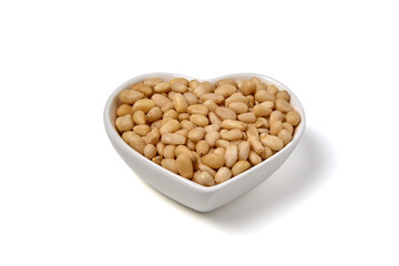 peeled pine nuts in a heart-shaped ceramic bowl isolated on white background.