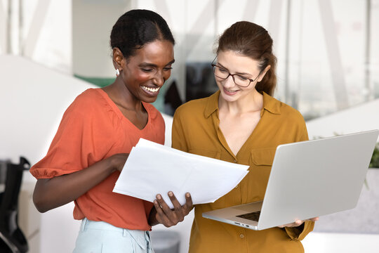 Fototapeta Happy young African American professional woman consulting financial or legal expert briefly, showing paper report to coworker, pointing at document, asking for advice, assistance, consultation