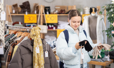 Interested teenage girl choosing gloves in the store, she came to the sale of winter clothes and accessories