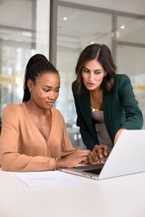 Young Latin mentor training new African employee at laptop, pointing at screen, explaining...