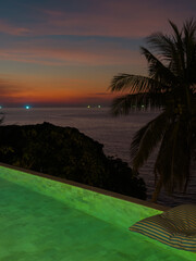 View from luxury villa at dusk, pool lighting, sun loungers for sunbathing, umbrellas from the sun, pillows for swimming in the pool, palm tree on background