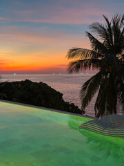 View from luxury villa at dusk, pool lighting, sun loungers for sunbathing, umbrellas from the sun, pillows for swimming in the pool, palm tree on background