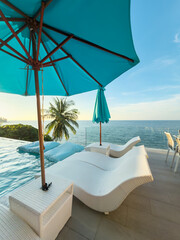 View from luxury villa at sunset, sun loungers for sunbathing, umbrellas from the sun, pillows for swimming in the pool, palm tree on background