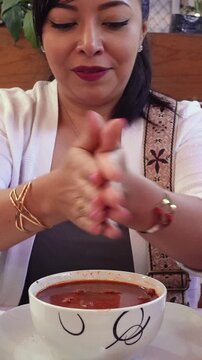 Mexican woman adding oregano to her food, a red stew. Menudo rojo.