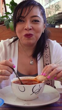 Mexican woman eating menudo rojo with tortillas. Red stew.
