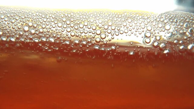 Stirring homemade Tepache drink with a spoon. Mixing orange fermented liquid foam close up.