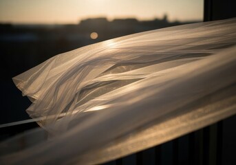A sheer white veil gently sways in the breeze during sunset. The soft fabric catches the warm light, creating a serene atmosphere.