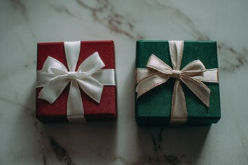 Two beautifully wrapped gift boxes, one red with a white ribbon and one green with a cream ribbon, arranged on a marble surface, perfect for New Year and Christmas celebrations