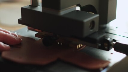 Leather embossing on hot stamping machine close up branding text pressed into brown hide for handmade wallet or case production