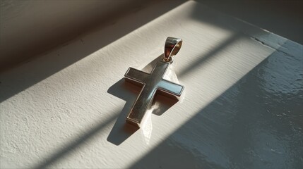 Silver cross pendant elegantly positioned on a smooth white acrylic surface, illuminated from the side to create striking long shadows and enhance its reflective qualities
