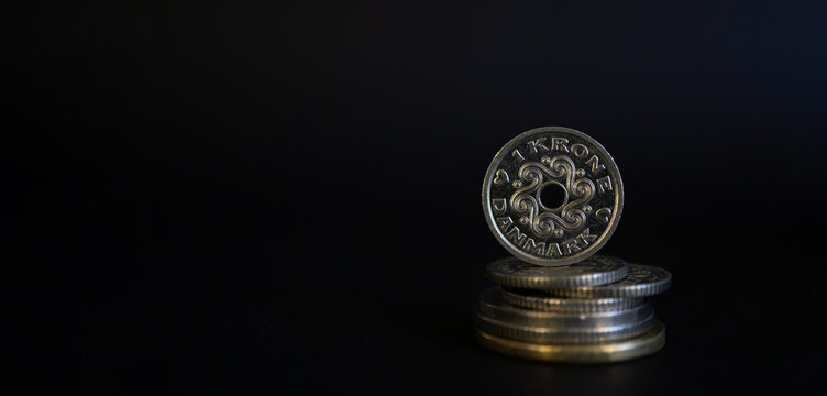 One Danish Krone Coin Balancing on Stack of Money Against Dark Background for Finance Concepts