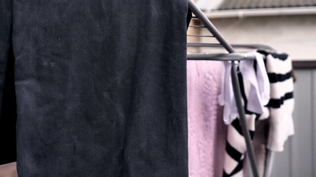 close-up focusing on the black fabric of the trousers hanging on the drying rack. The visibility of the white residue streaks , clearly illustrating the issue caused by undissolved washing powder. 