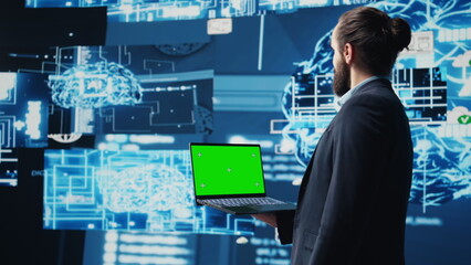 Business AI expert holding green screen on device next to brain animation, ensures implementing neural networks system. Young specialist analyzing algorithms and coding tools. Camera B.
