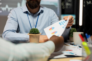 Close up of diverse business team meeting after hours for visual data reports, reviewing infographics and projections while sharing files to establish finance objectives. Business intel forecasting.