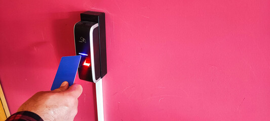 A card reader on a red wall, a hand with a card reaching for the card reader. Concept of modern reading devices