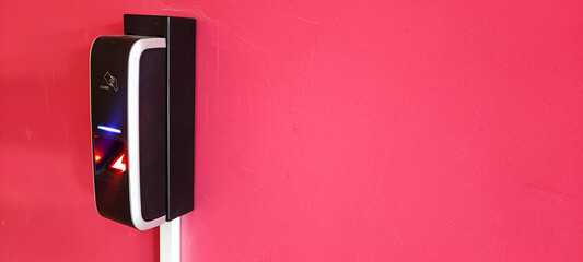 A card reader on a red wall, a hand with a card reaching for the card reader. Concept of modern reading devices