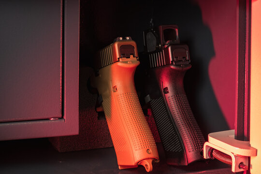 Modern handguns, one black and one tan, stored securely in a dimly lit gun safe, emphasizing firearm safety and home protection.