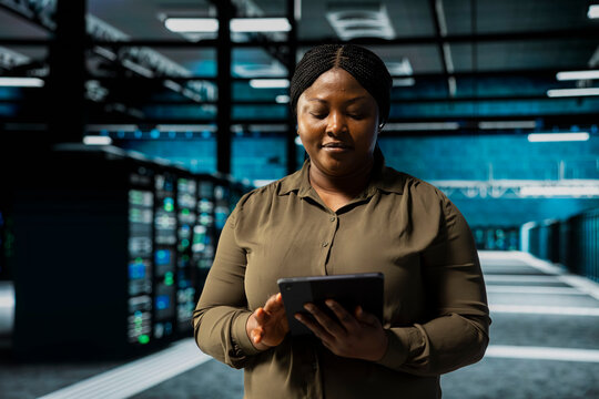 Woman uses tablet to implement security measures integral to fortifying data center defenses against cyber threats. African american server hub worker doing threat detection, defending company systems - Powered by Adobe