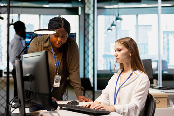 Manager supervising young employee in startup office, reviewing code scripts on computer. African american tech company supervisor overseeing work by trainee doing software development