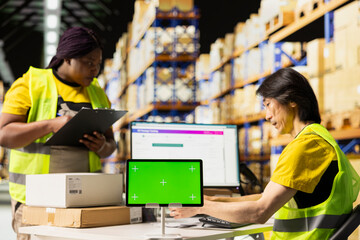 Multiethnic team of warehouse workers next to green screen monitor. Managing shipping labels, barcode scanner data or e-commerce inventory tracking systems in industrial warehouse.