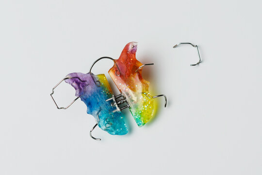 Colorful orthodontic retainer lies broken on white background, symbolizing dental care problem and need for timely appliance repair