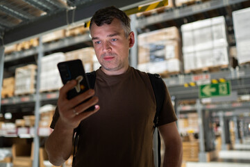 Warehouse worker checking information on smartphone in a storage facility aisle