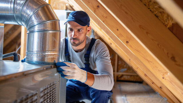 Hvac technician installing metal duct in attic among wooden beams, ventilation system installation workflow, gloves cap overalls tools ductwork handling airflow management
