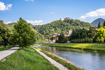 Waterfront of the Savinja river (Savinjsko nabrezje) with Celje Castle on the hilltop and a green urban landscape in Celje, eastern Slovenia.