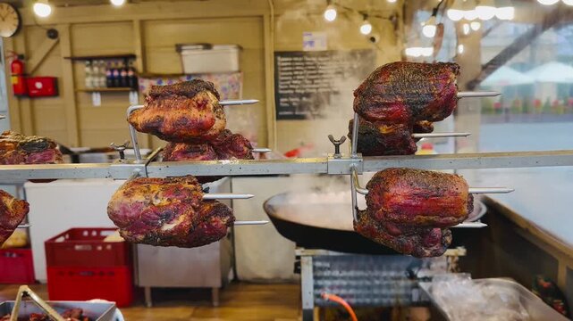 Roasted pork cooking on rotating skewers at an outdoor Christmas market stall, surrounded by warm lights and rustic decor.