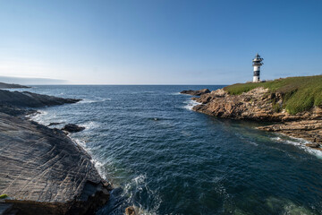 wide angle view of a modern black and white lighthouse standing on a rocky cliff by the deep blue sea under a clear sky, Isla de Pancha, Ribadeo, Galicia, Spain,
