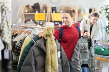 Teenage girl buyer choosing warm plaid coat in clothing store