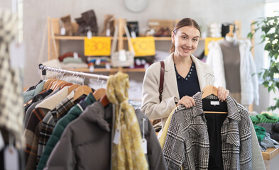 Fototapeta premium Adult woman buyer choosing warm plaid coat in clothing store