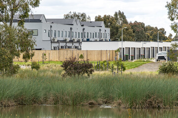 Modern townhouses in Point Cook, Melbourne, overlooking wetland reeds and landscaped green space. Concept of suburban&ndash;nature interface, urban conservation, contemporary Australian neighbourhood