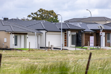New single-storey homes in an outer-suburban Melbourne estate bordered by vacant grassland. Concept of urban expansion, residential development, suburban housing market, and undeveloped land buffer