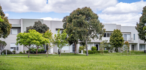 Modern residential townhouses in Point Cook, Melbourne, framed by a green verge and established street trees. Concept of suburban planning, landscaped public open space,Australian neighbourhood living