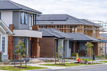 New estate housing development in suburban Melbourne, showing completed modern homes alongside an active construction site with timber framing and roofing works. Housing boom, urban expansion