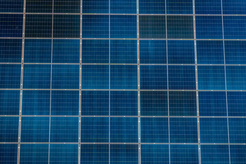 Solar panels arranged in grid pattern on building roof during daylight hours near urban area