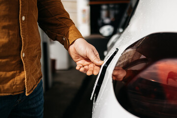 A man in a brown shirt refueling a white car at a gas station, demonstrating the everyday experience of car servicing.