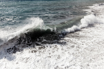 Fototapeta premium Powerful ocean wave crashing onto sandy shore, creating frothy white foam, with glistening water reflecting sunlight, embodying the beauty of nature's force and tranquility
