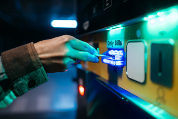 Hand of an individual inserting a card into a payment machine, illuminated by blue and green lights, showcasing modern technology in a public transport setting