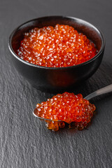 Red caviar in bowl with spoon on black background