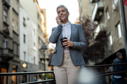 Confident businesswoman communicating on mobile phone in city - Powered by Adobe